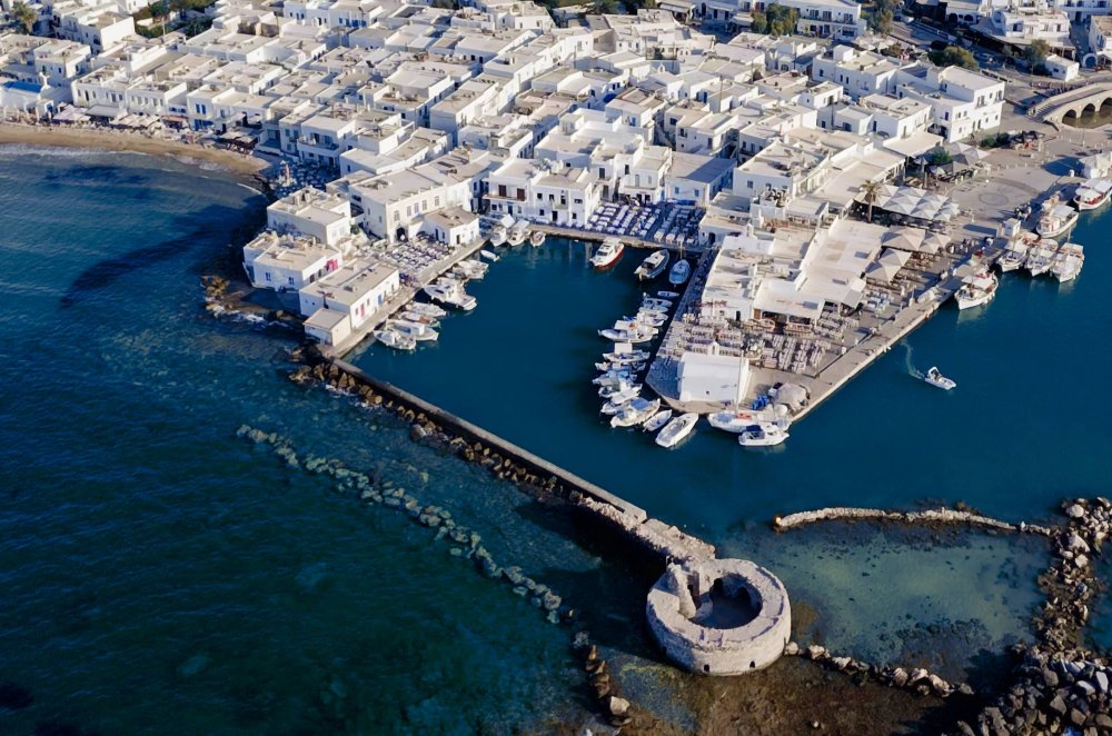 Aerial view of the little Venetian port of Naoussa, Paros, framed by the white village and turquoise bay